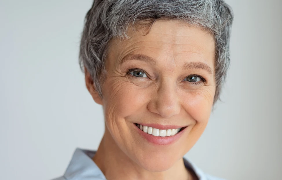 Mature woman with short gray hair smiling at the camera after her Dental Implant surgery.