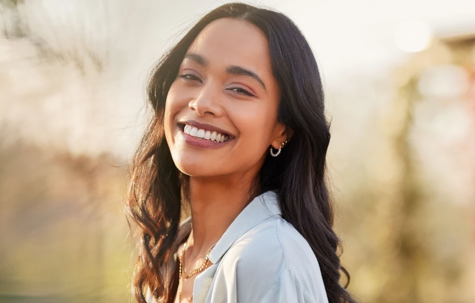 A smiling woman with sunlit hair outdoors showcases her dental health.